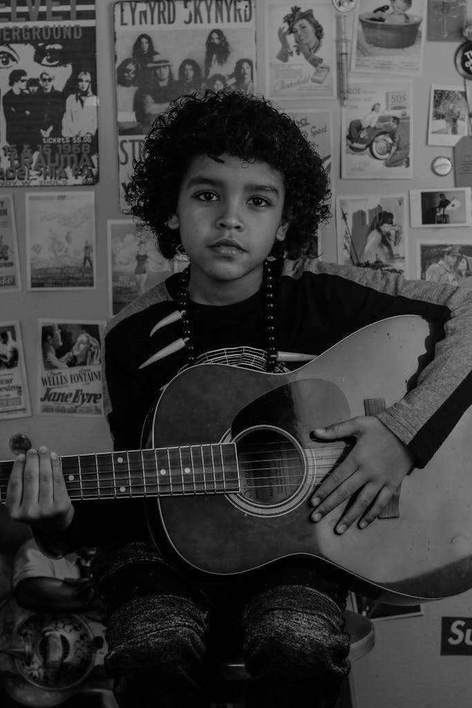 Black and white of African American boy guitarist with acoustic guitar and Afro hairstyle looking at camera